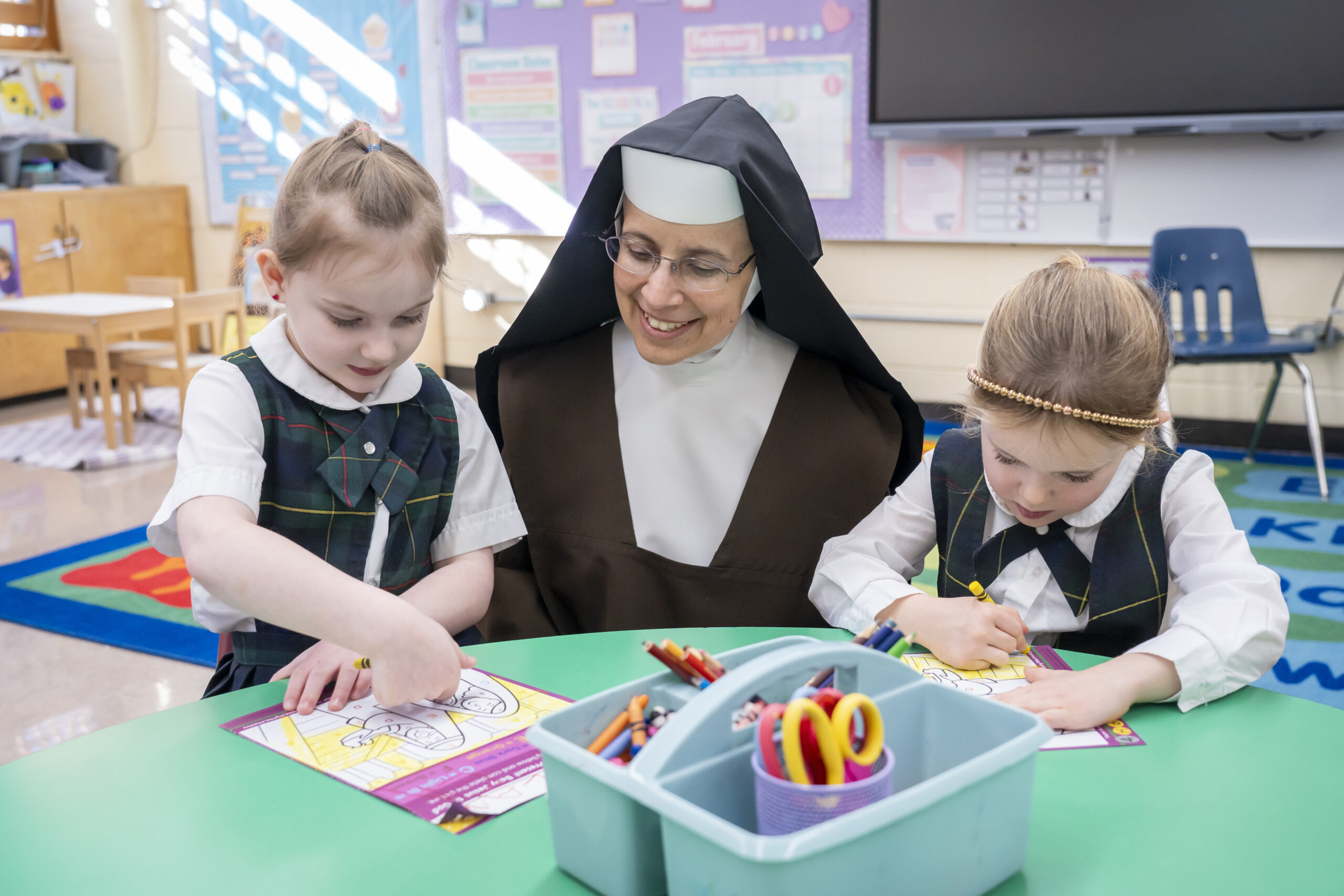 A sister in a brown habit helping two girl students in green plaid uniforms.