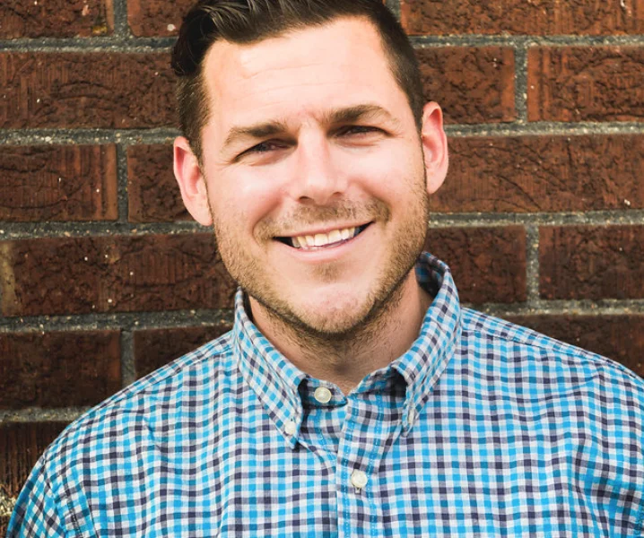 A man in a blue plaid shirt against a red brick wall.