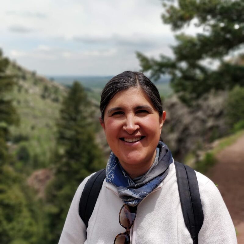 A woman with dark hair and a white sweatshirt hiking in the Rockies.
