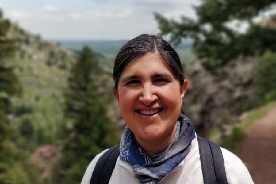 A woman with dark hair and a white sweatshirt hiking in the Rockies.