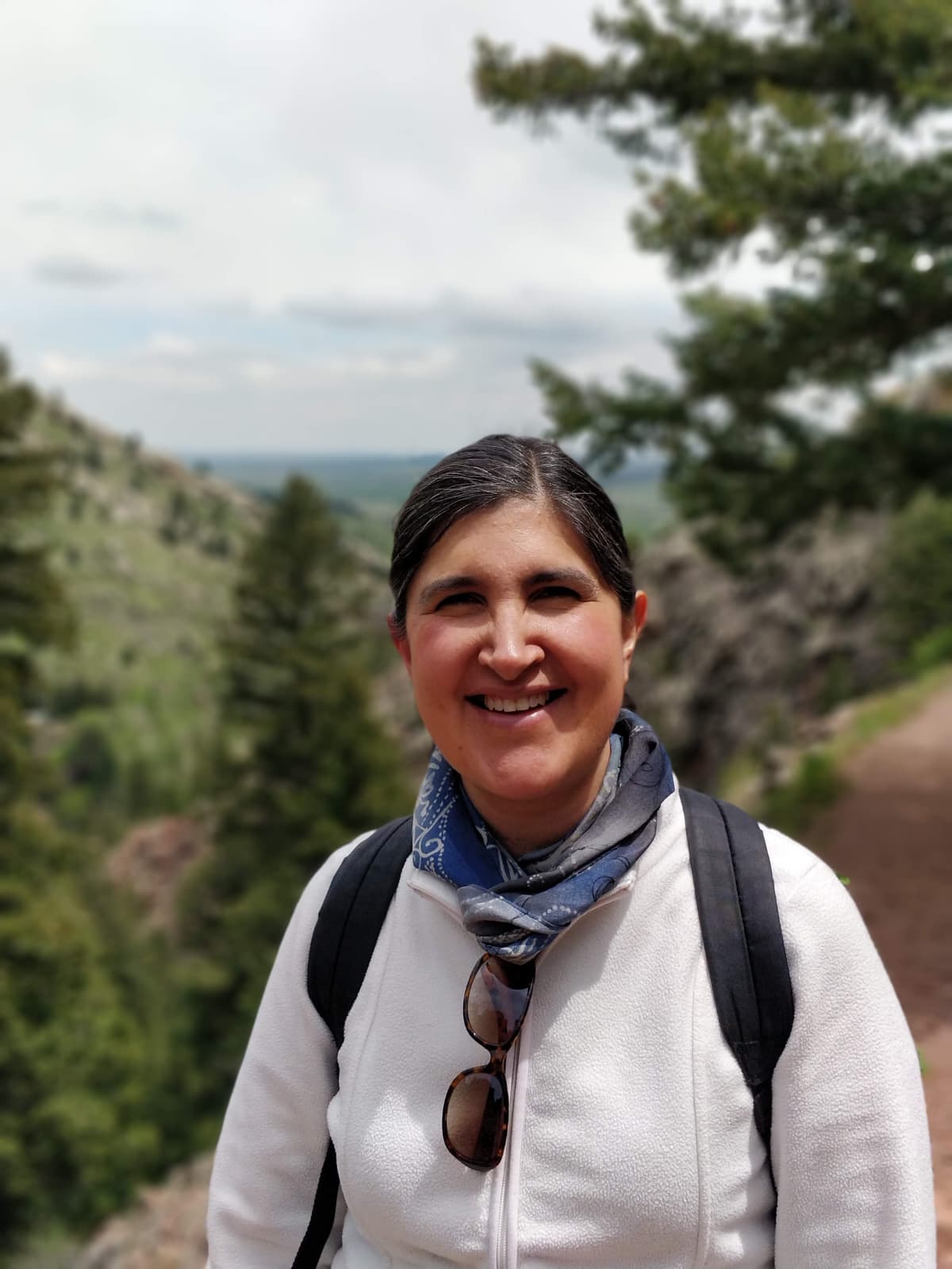 A woman with dark hair and a white sweatshirt hiking in the Rockies.