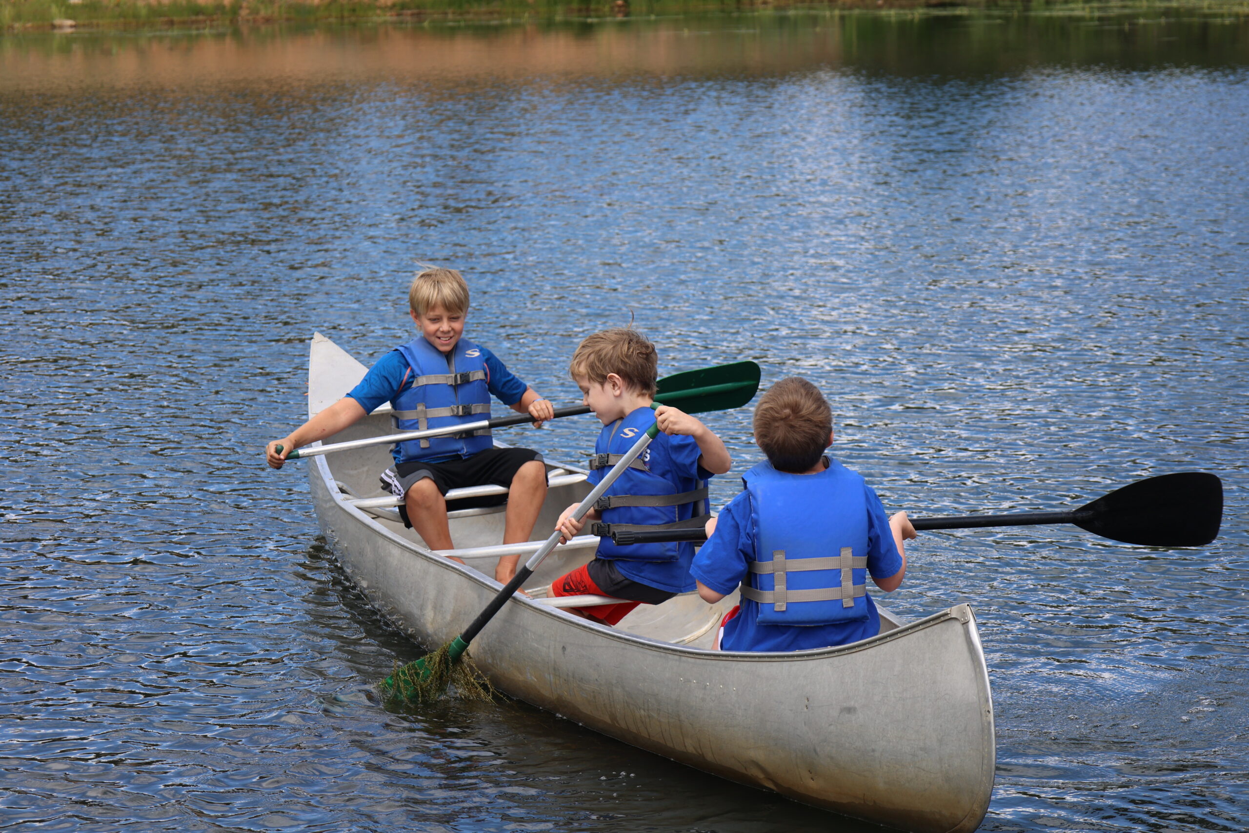A group of 3 boys canoeing on a lake
