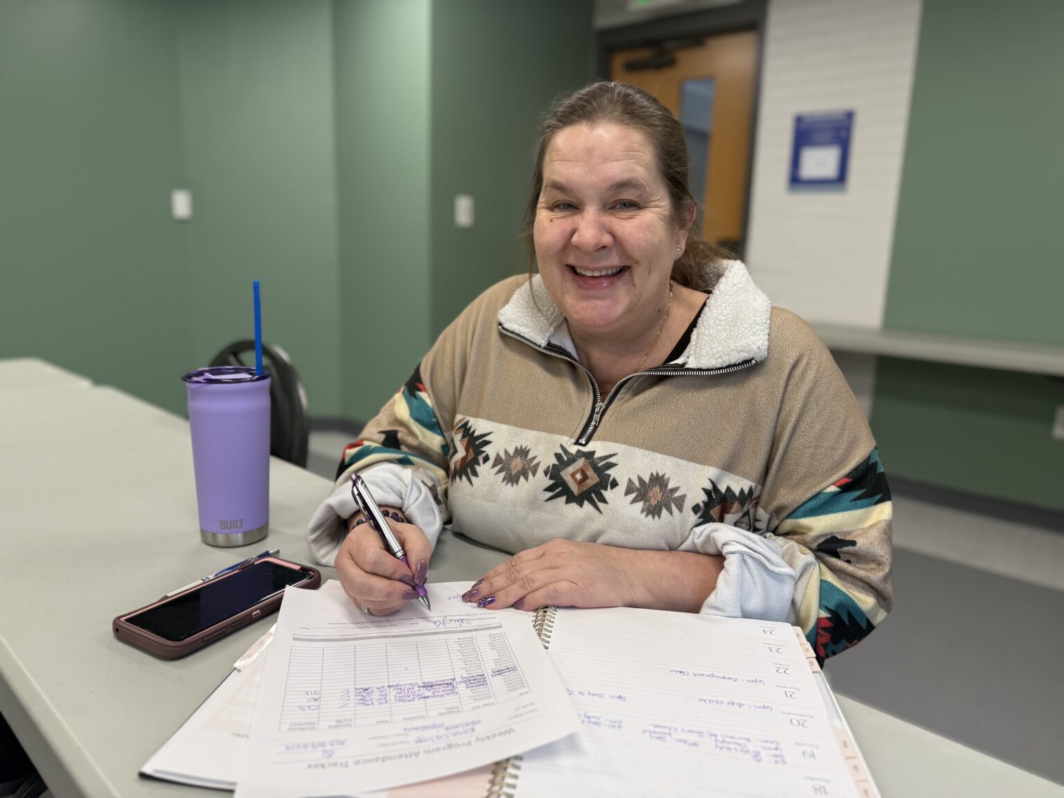 A woman with a winter sweater signing paper work for a parenting class.