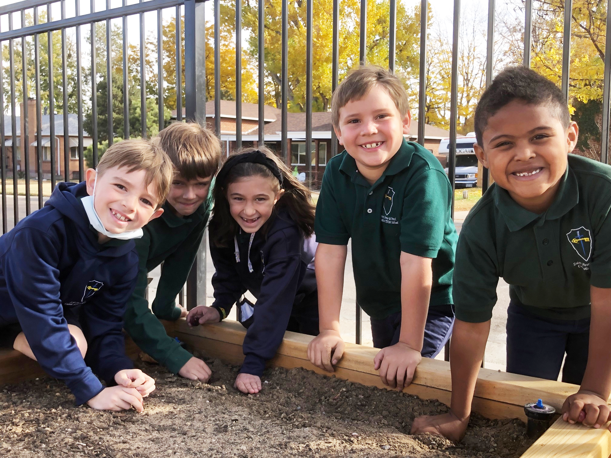 A group of kids gathered around a sand box outside smiling.
